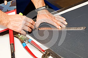 A worker marks out a sheet of roofing iron with a pencil and a metal ruler. Close-up of a worker`s hands