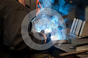 Worker in mask, in the process of welding metal with bright light, smoke and sparks