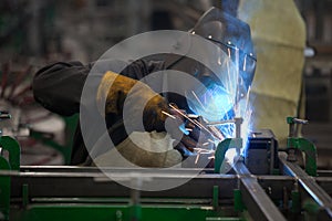 Worker in mask, in the process of welding metal with bright light, smoke and sparks