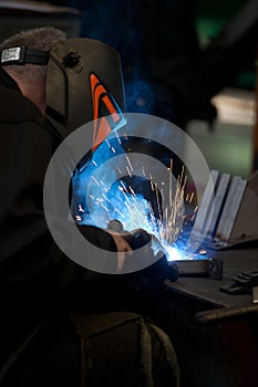 Worker in mask, in the process of welding metal with bright light, smoke and sparks