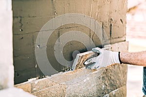 Worker mason closely placing stone tile on vertical wall. Industry details - construction site