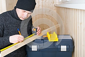Worker, measures a wooden bar with a tape measure, a simple pencil
