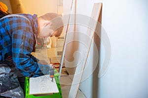 Worker measuring and marking laminate floor tile for cutting