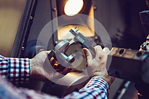 Worker measuring threaded part with caliper inside a CNC machine