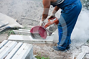 A worker mends part of the road, cuts out worn asphalt in a cloud of dust using a portable concrete cutter and a cutting