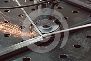 Worker in metal factory grinding workpiece with sparks flying