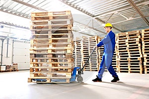 Worker moving wooden pallets with manual forklift in warehouse