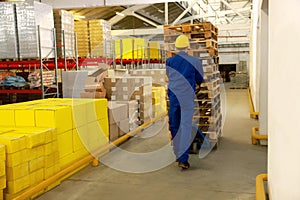 Worker moving wooden pallets with manual forklift in warehouse, back view