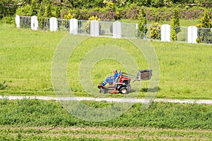 Worker mowing grass in city park. Sunny summer day.Mature man driving grass cutter in a sunny Gardener driving a riding lawn mower