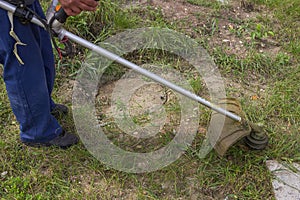 Worker mowing the grass with gas string trimmer