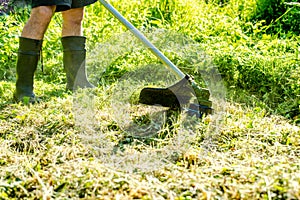 Worker mowing tall grass with electric or petrol lawn trimmer in city park or backyard. Gardening care tools and equipment