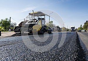 Worker operating asphalt paver machine during road construction and repairing works. A paver finisher, asphalt finisher