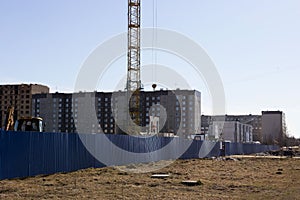 A worker in an orange helmet directs the unloading of concrete slabs with a crane on the construction site of a multi-storey multi