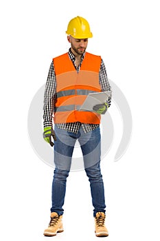 Worker in orange reflective waistcoat and white helmet is standing with documents and looking at it