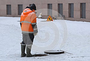 A worker in an orange uniform stands over an open sewer