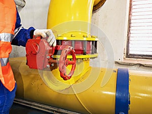 Worker in orange warning vest  turning wheel of valve in industrial factory