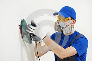 Worker with orbital sander at wall filling photo