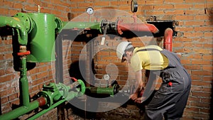 The worker in the overalls closes the water valve. The man turns off the heating in the boiler room.