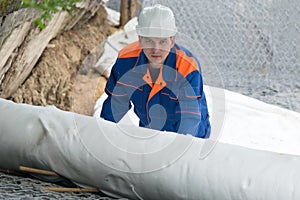 A worker in overalls covers stones and iron mesh with white wrap