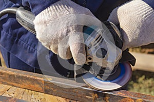 A worker in overalls is grinding a weld seam