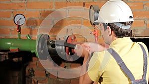 A worker in overalls opens the water valve. The man includes heating in the boiler room. Close-up