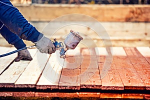 Worker painting brown timber, renovating exterior wooden fence. Worker using spray gun photo