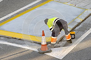 Worker painting a curb on a city road with a roller and yellow paint