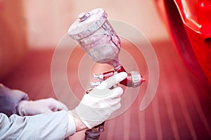 Worker painting a red car in painting booth using spray gun