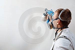 Worker painting wall with spray gun in white color.