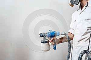 Worker painting wall with spray gun in white color.