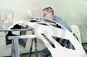 Worker painting white car bumper.