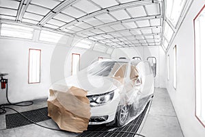 worker painting a white car in special garage, wearing costume and protective gear