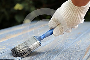 A worker painting a wooden wall. A man holding brush. A hand of worker painting wooden plank. A painter with paint brush