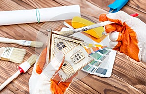 Worker paints model of house over table with brushes, color swatches book and paint roller. Home improvement concept