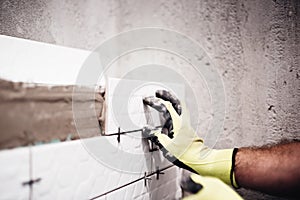 Worker placing small ceramic tiles with plastic spacer on bathroom walls