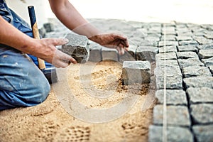 Worker placing stone tiles in sand for pavement, terrace. Worker placing granite cobblestone pavement at local terrace