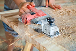 Worker planing a table top of wood with a electric plane