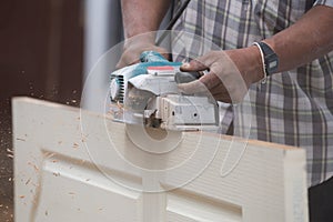 Worker planing a wood of door with electric plane