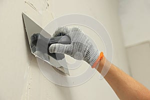 Worker plastering wall with putty knife indoors, closeup