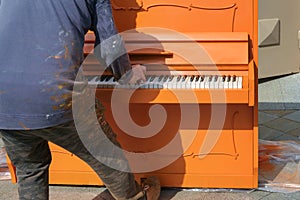 A worker is playin a orange new painted piano