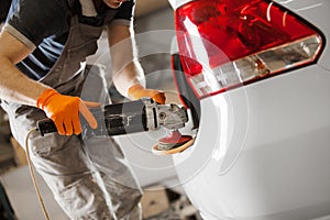 Worker polished white car with orbital polisher in auto repair shop, close-up. Vehicle detailing.