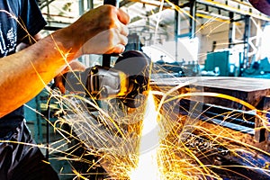 The worker polishes the metal with a grinding machine and sparks close-up.