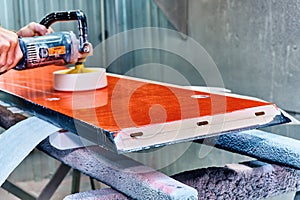 Worker polishes a red panel with a grinder. Woodworking and carpentry production. Furniture manufacture.