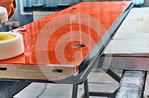 Worker polishes a red panel with a grinder. Woodworking and carpentry production. Furniture manufacture.