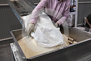 A worker pours a bag of sugar onto a conveyor line for further processing