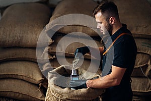 Worker pours a scoop of coffee into a device for measuring humidity from a bag, in the background of a warehouse