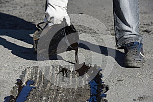 A worker pours tar on the road with a bucket.