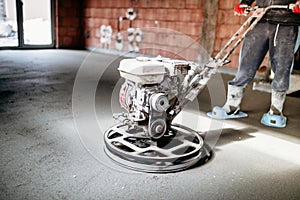 Worker with power trowel tool finishing concrete floor, screed, smooth concrete surface photo