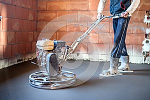 Worker with power trowel tool finishing concrete floor, smooth concrete surface at house construction