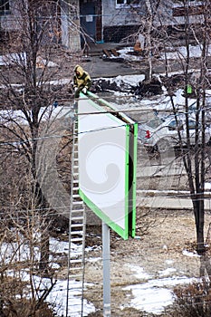 Worker prepares billboard to installing new advertisement. Industrial climber working on a ladder - placing